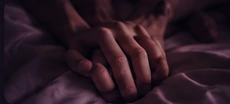 Hands intertwined on dark bedding